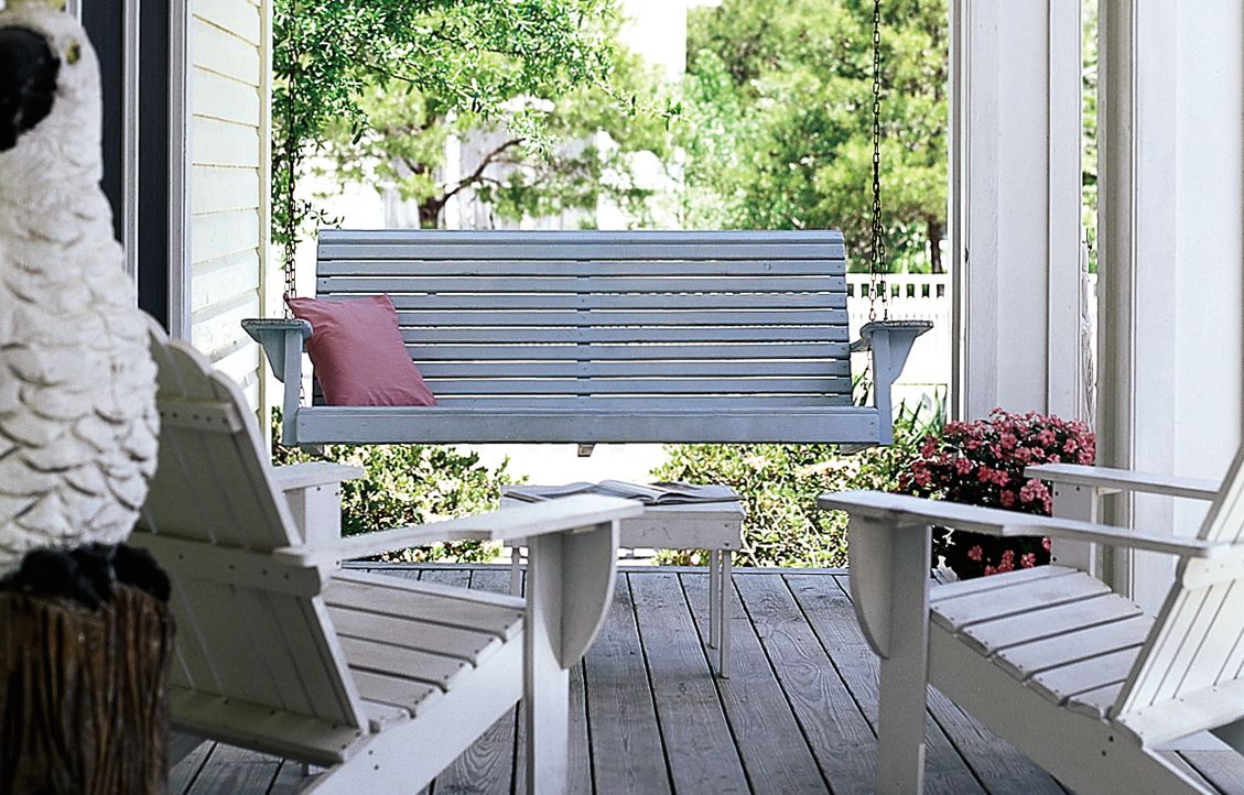 A green porch swing hanging above a wooden porch, across from a pair of deck chairs.