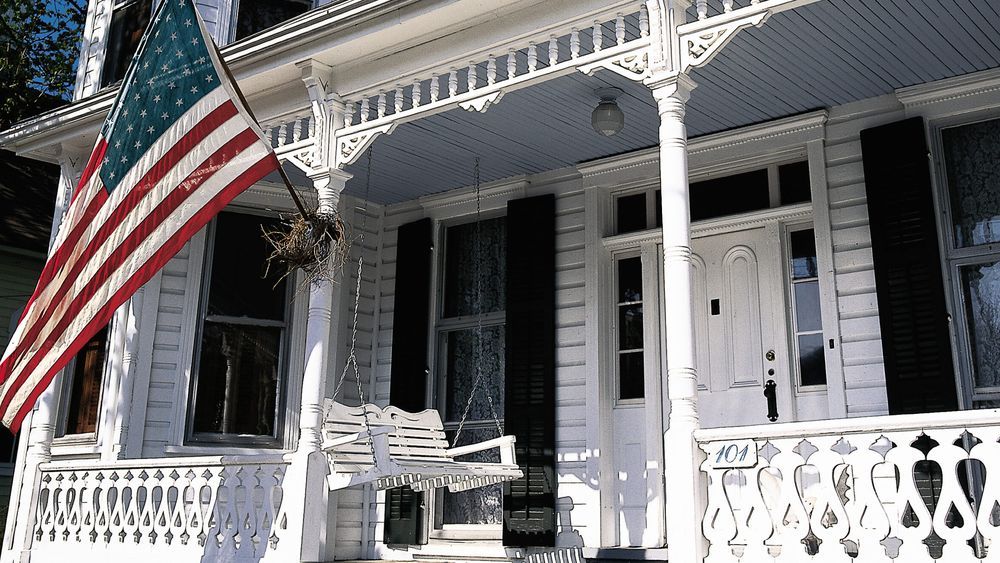 A white porch swing hanging below a large American flag.