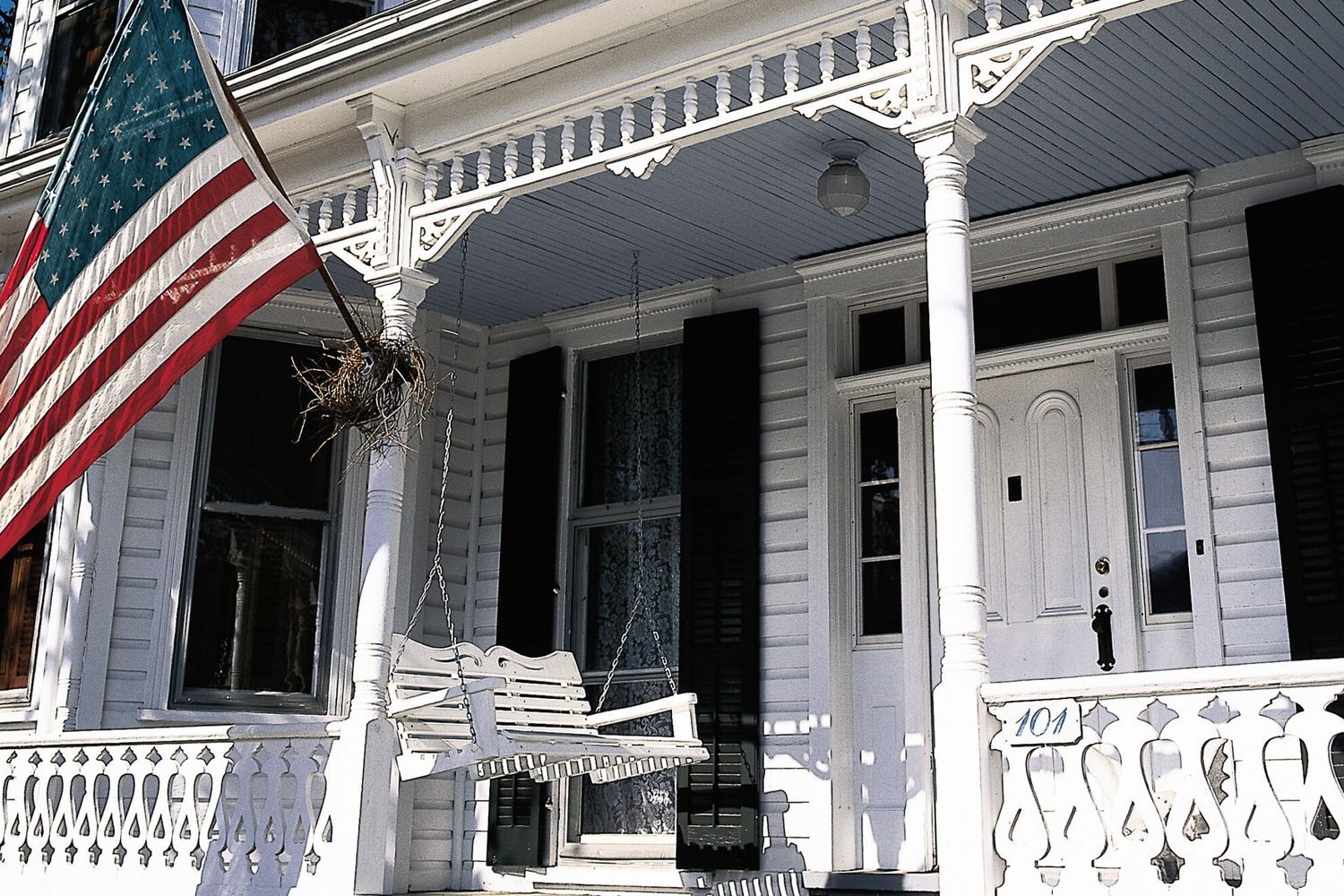 A white porch swing hanging below a large American flag.