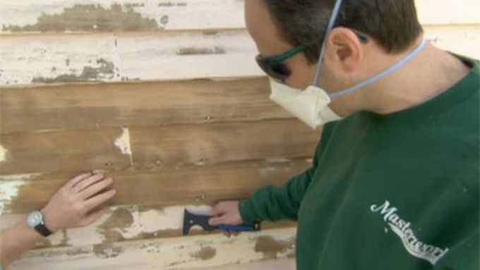 A man scraping paint off the exterior of a wall to prepare to apply a new paint.