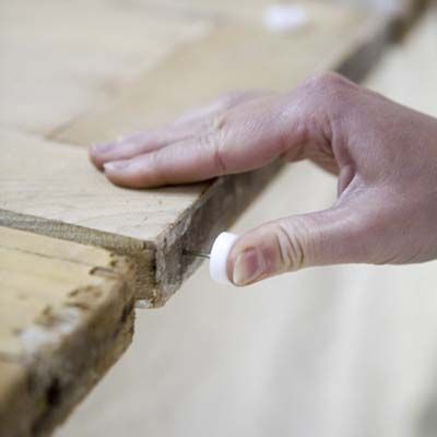 Hand installing soft vinyl furniture glides on the bottom corners of the shutters