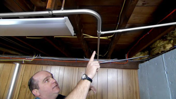 A man pointing to a noisy pipe on a ceiling.