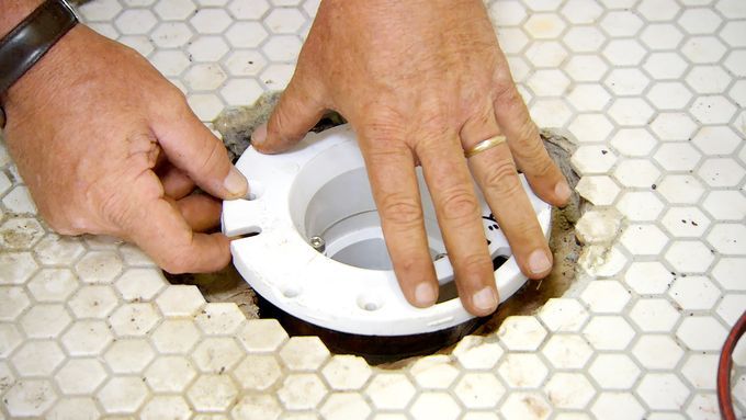 A man installing a toilet flange in a bathroom.