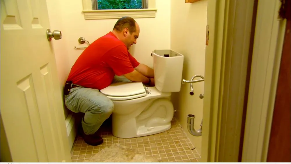 A man working on a toilet with the lid removed.