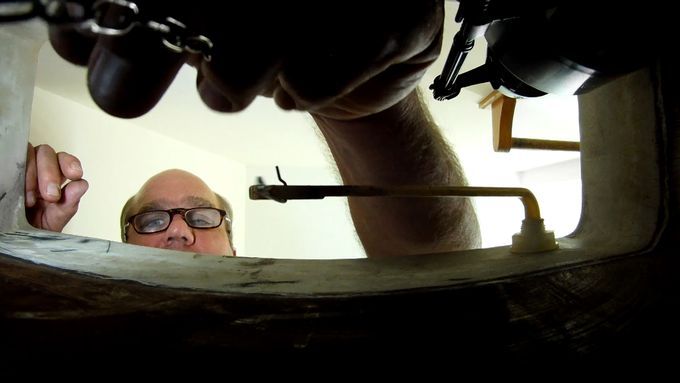 A man peering into and repairing a noisy toilet.