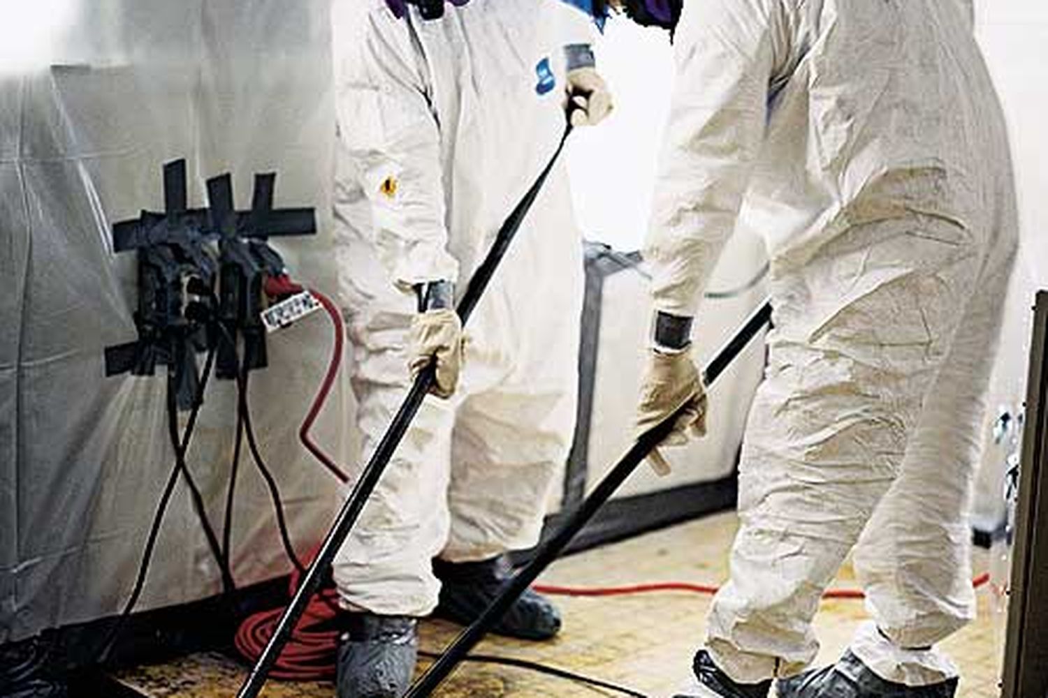 Two men in an asbestos abatement crew removing asbestos from the floor of a home.