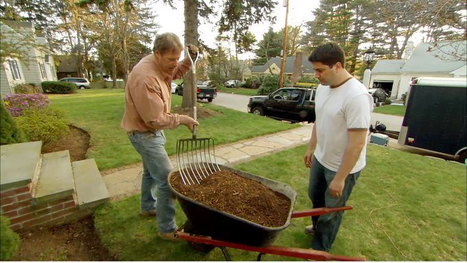 A man using a pitchfork to remove mulch from a wheelbarrow.