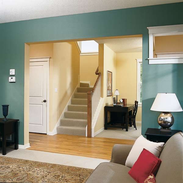 Blue-green painted living room looks through square archway into an entryway painted a yellow color.