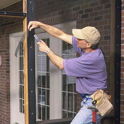 A man trims away the excess of his proch screen.