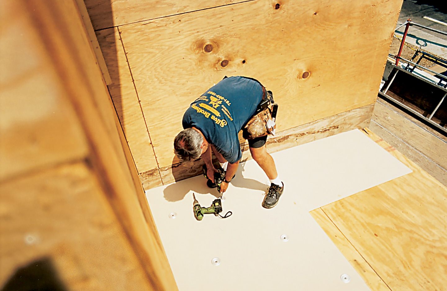 A man using a drill to apply a roofs underlayment.