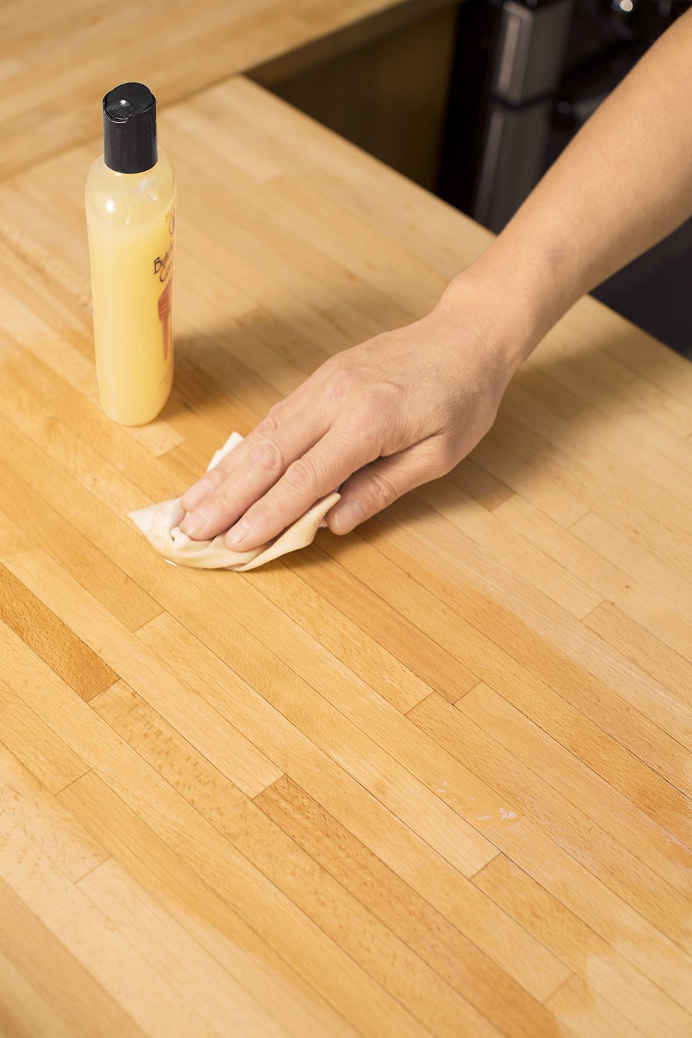 A hand wiping a rag soaked in butcher block conditioner on a butcher block countertop.