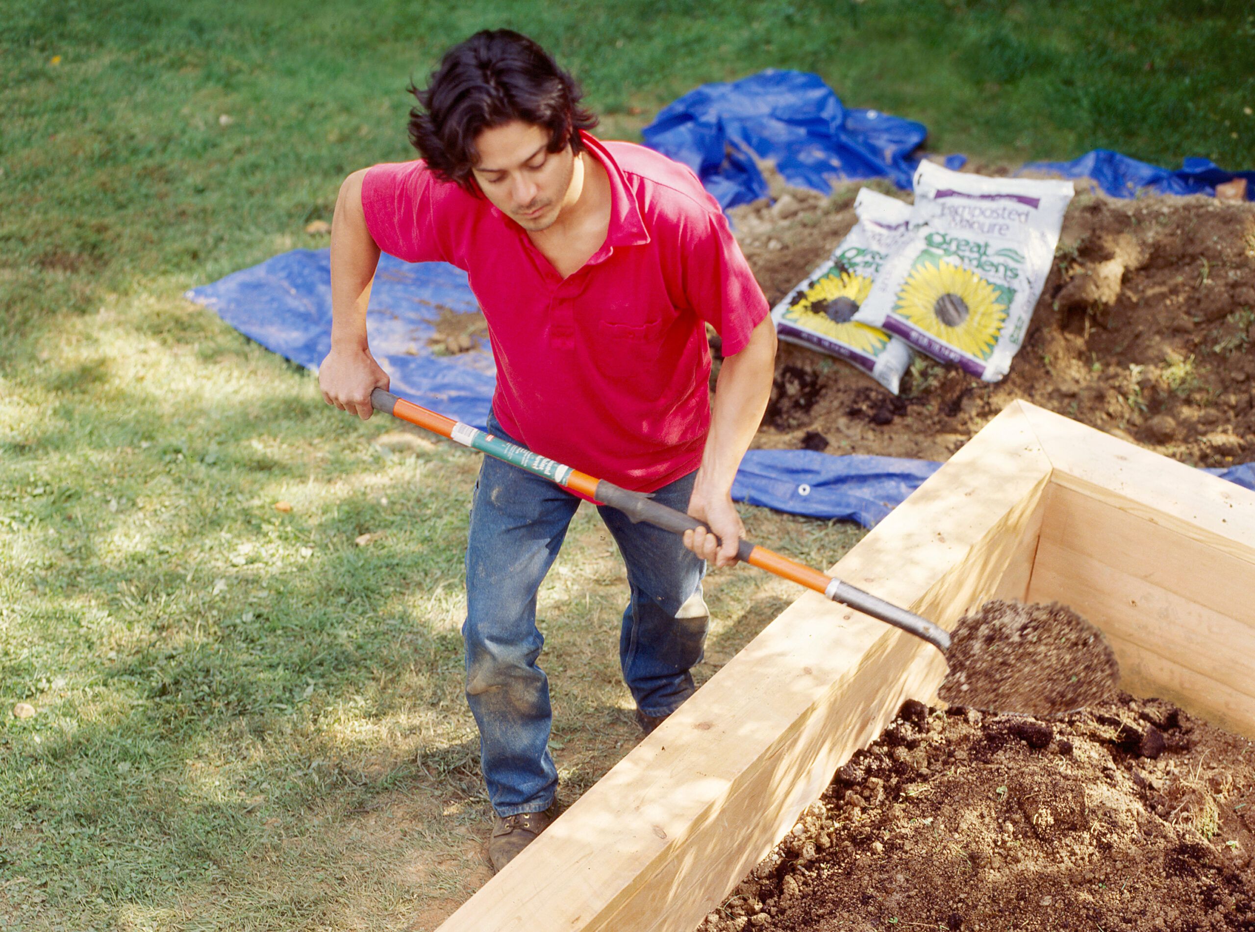 A man shoveling soil into a garden bed.