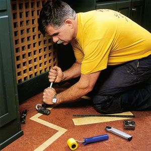 A man using a roller to work on linoleum flooring in a home.