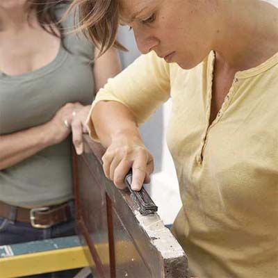 Two person remove old hardware from a shutter to make it a cabinet door.