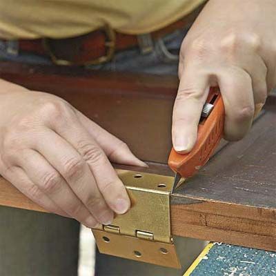 A person uses a box cutter to make where the cabinet hinges will go on the shutter.