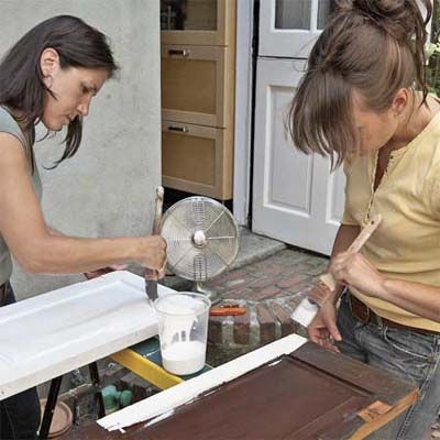 Two people paint shutter cabinets white.