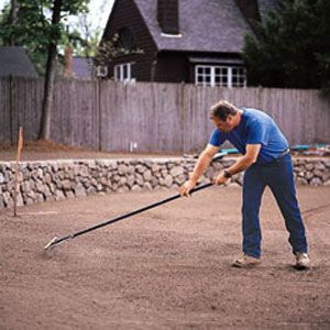 A person using an iron rake to rough grade the soil.