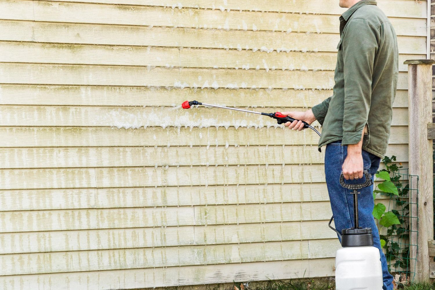 A man spraying siding with a power washer to remove mildew.