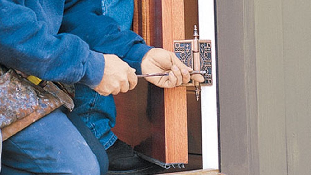 A man using a screwdriver to work on a sticking wooden door.