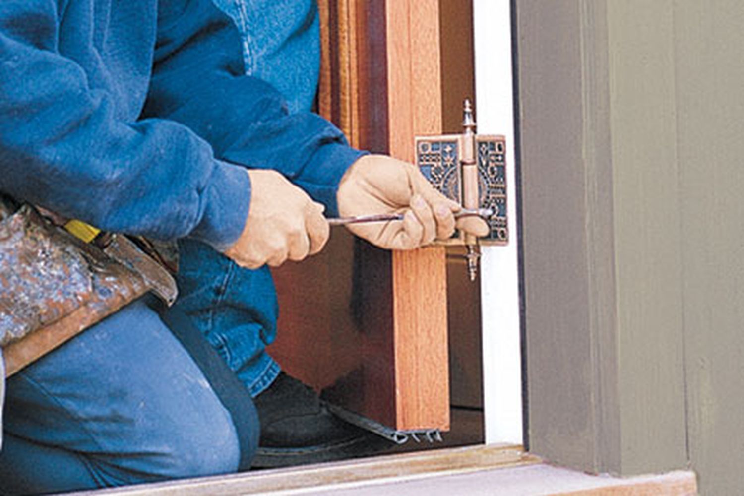 A man using a screwdriver to work on a sticking wooden door.