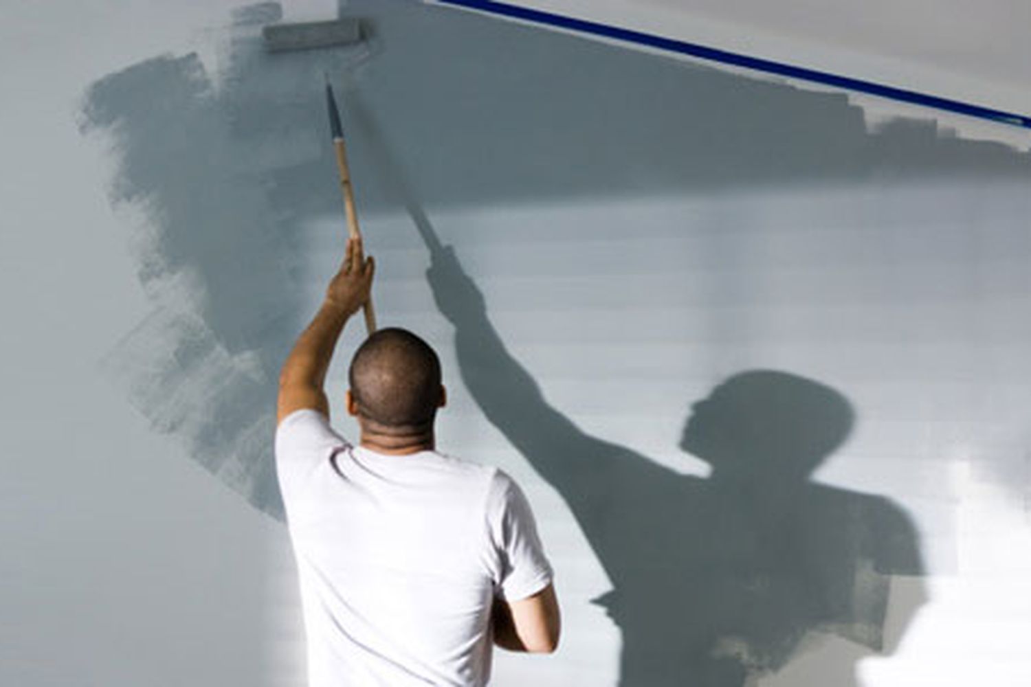 A man using a paint roller to paint a wall.