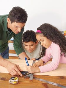 Man with kids measuring wooden pieces for step stool.