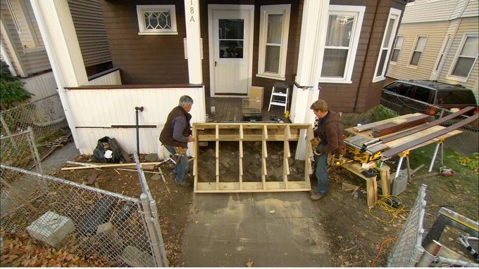 Two men installing wooden stairs up to a porch.