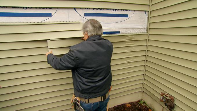 A man working on repairing vinyl siding on a house that has melted.