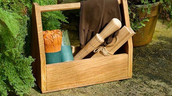 A wooden garden tool-tote with tools resting inside of it.