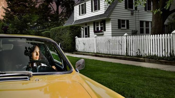 A car in front of a home with a lightning strike in the background.