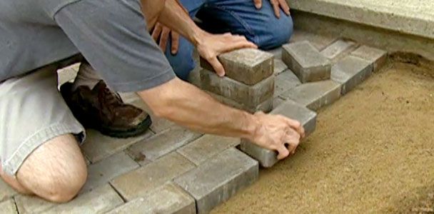 Two men laying down grey bricks for an outdoor pathway.