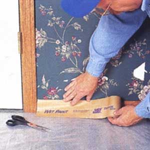 A man using masking paper to protect the baseboard of a wall.