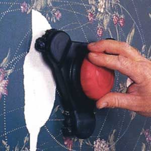 A person using a scoring tool to perforate a piece of wallpaper.