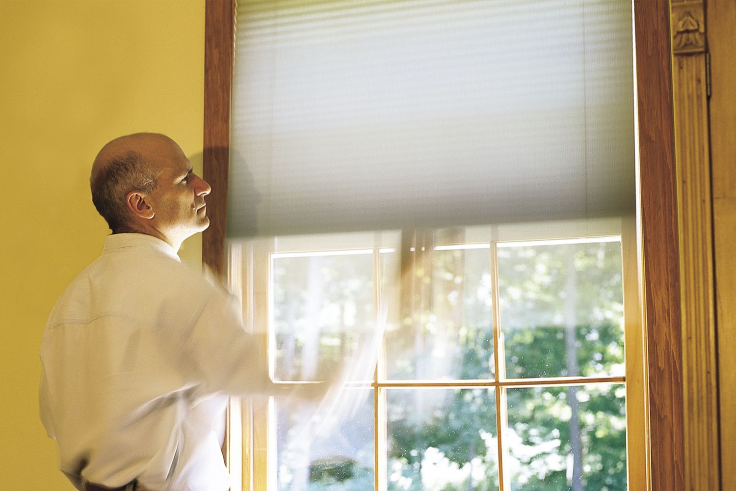 A man testing window shades to ensure they are operating correctly.
