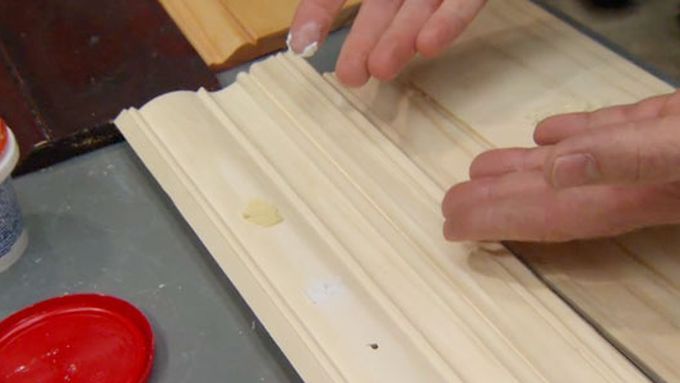 A man applying wood filler to a piece of molded wood.