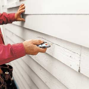 A man using a knife to cut wood siding.