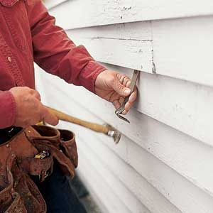 A hammer and crowbar used to pry off a piece of wood siding.