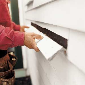 A man snapping off a piece of wood siding from a building.