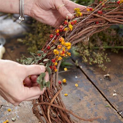 Someone adding berries and eucalyptus to the base of a wreath.