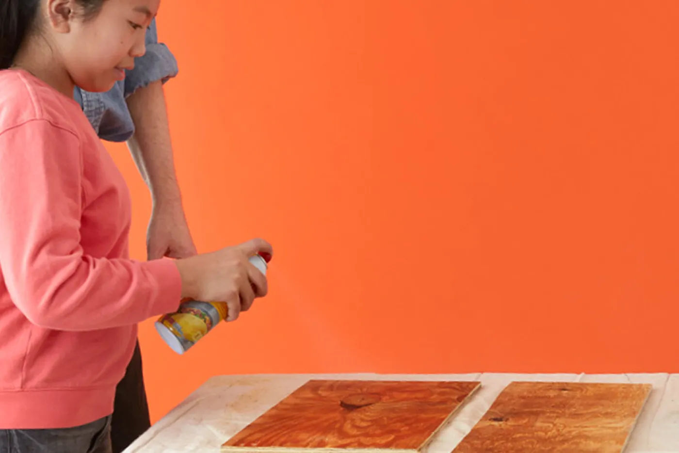 A child coating the wood panels with cooking spray.