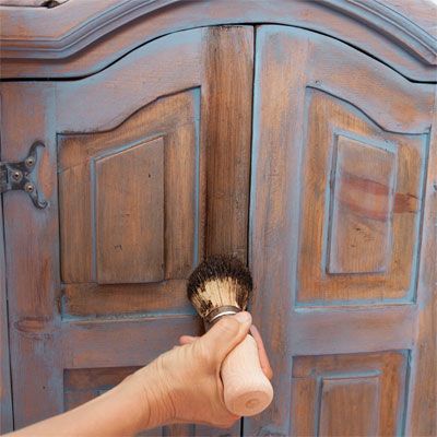 A person using a wax brush on a recently color washed cabinet.