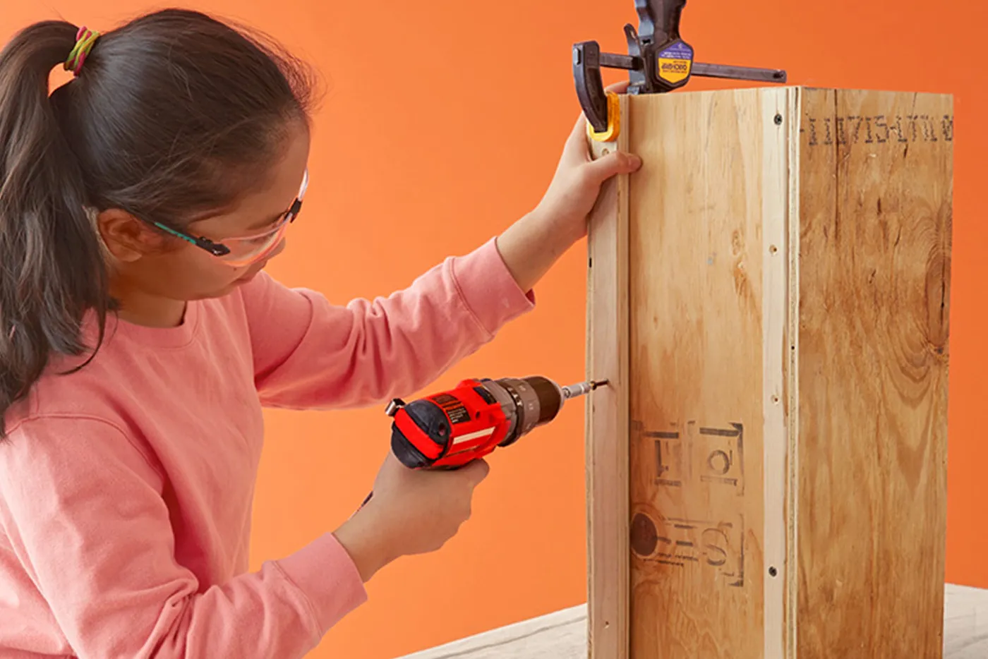 A child building a form by securing the strips of plywood with screws.