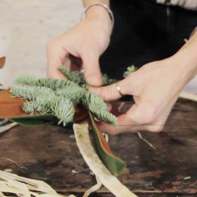 A woman constructing a wreath out of evergreens.