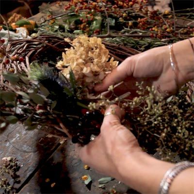 A woman adding dried flowers to a wreath.