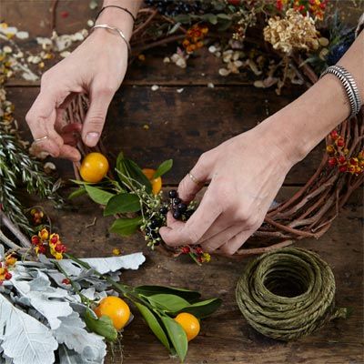 A woman adding small citrus fruits to a wreath.