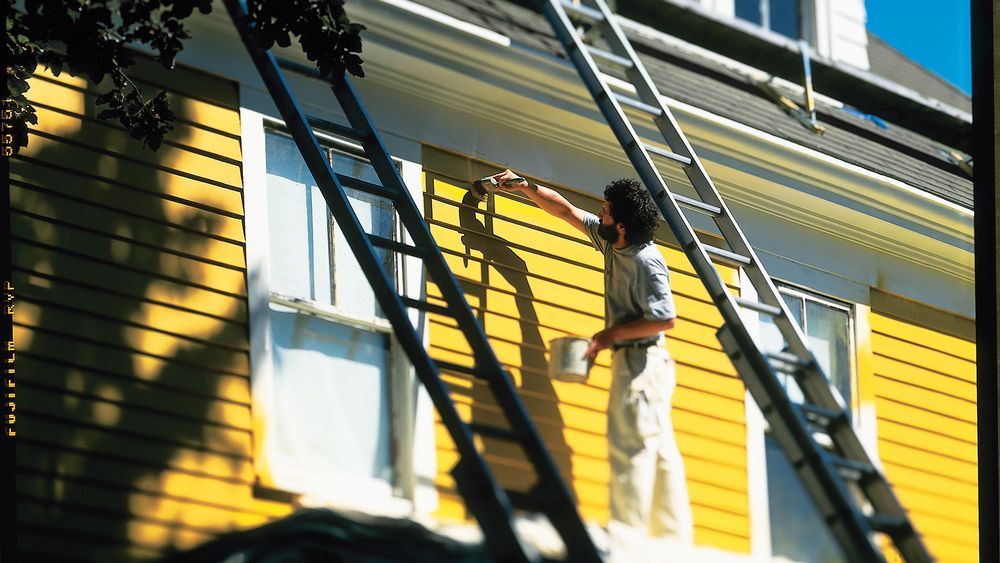 Professional painter painting the exterior siding of a house the color yellow.