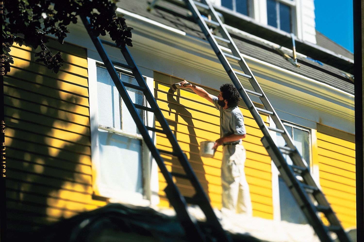 Professional painter painting the exterior siding of a house the color yellow.