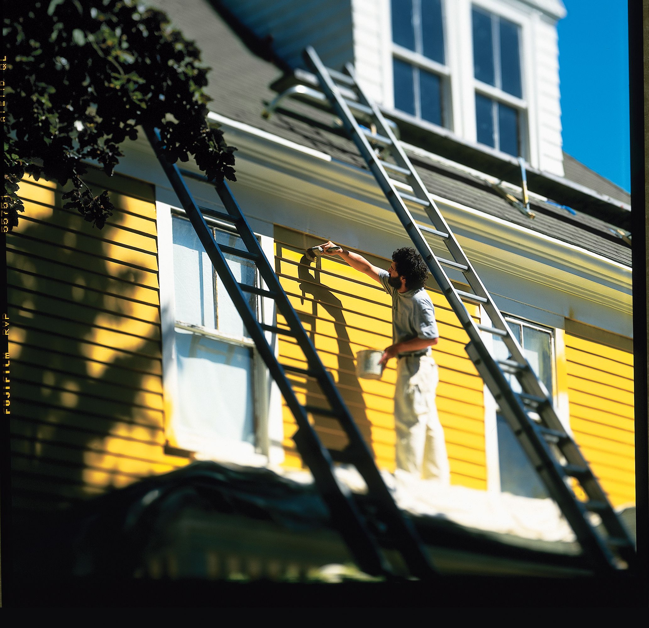 Professional painter painting the exterior siding of a house the color yellow.