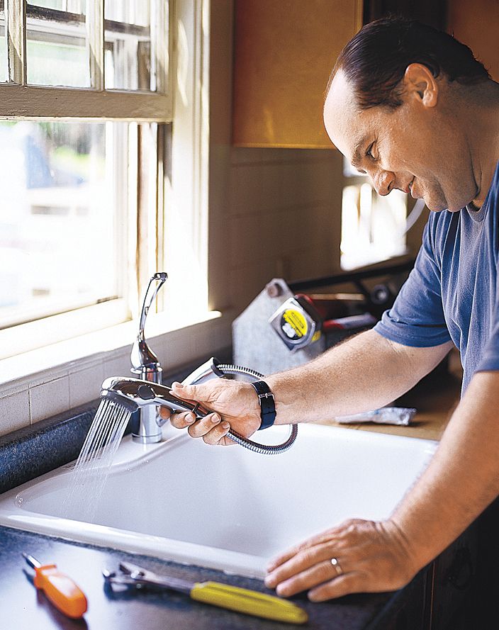 A man using the spray function of a stainless steel kitchen faucet.