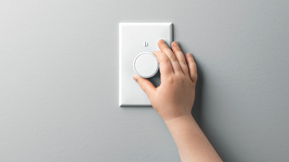 A hand turning the dial on a light dimmer switch.